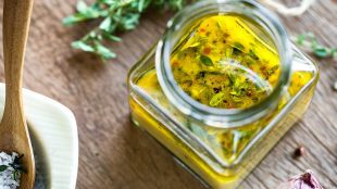 Image shows a jar of vinaigrette with some ingredients surounding it - garlic, herbs, salt