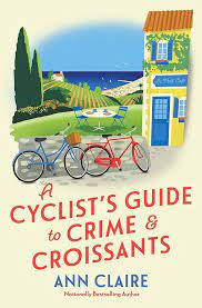 The book cover of a cyclists guide to crime and croissants. Shows two drawings of bikes in front of a yellow house by the ocean.