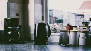 Image of an electric kettle and coffee machine on a kitchen counter, beside a window and jars of tea and coffee.