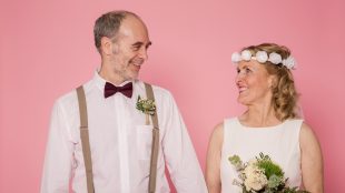 Middle aged couple looking at each other on a pink background, dressed for a wedding. Avoid wedding mistakes article Silver Magazine www.silvermagazine.co.uk