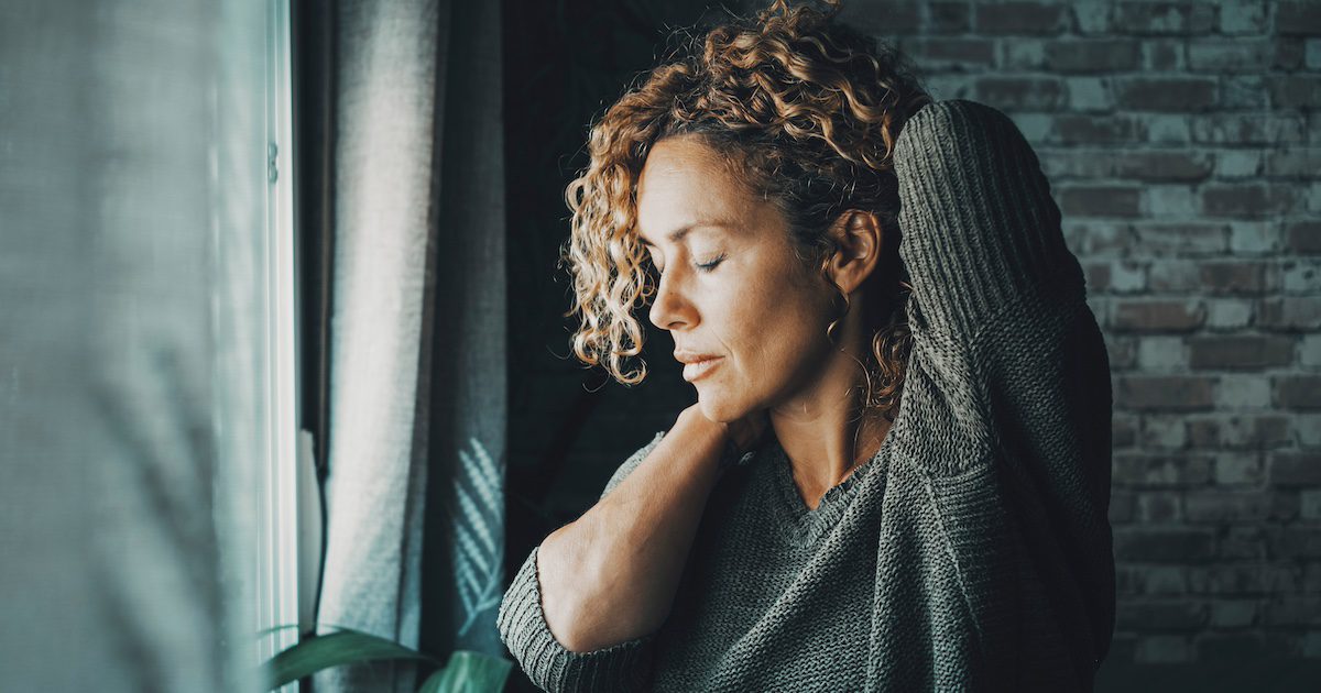 woman looking out the window, stretching her arms around her back, looking stressed out