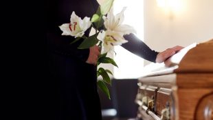 people and mourning concept - woman with white lily flowers and coffin at funeral in church