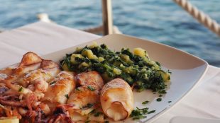 Grilled squid with boiled potatoes and chard (blitva) on white plate with sea on background. Traditional Croatian food. Rovinj/ Croatian food from Istria - article Silver Magazine www.silvermagazine.co.uk