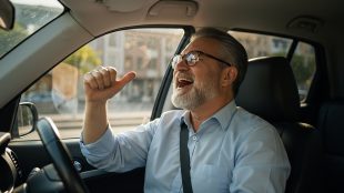 Joyful Mature Man Singing Along to Music While Driving His Car on a Sunny Day. Dad Rock driving playlist - Silver Magazine www.silvermagazine.co.uk