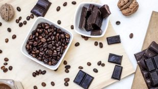 Cubes of dark chocolate and chocolate beans scattered across a wooden board. Benefits of dark chocolate on Silver Magazine.