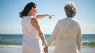 Image of a two women, one a young-adult and one elderly, holding hands and looking at the sea.
