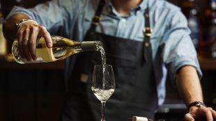 Male sommelier pouring white wine into long-stemmed wineglasses. Waiter with bottle of alcohol beverage. Bartender at bar counter pour elite drink into long-stemmed glass. English wines roundup feature on Silver Magazine www.silvermagazine.co.uk