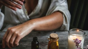 Pic shows arm of person dripping essential oil, with candle and nice oil containers in the foreground. Essential oils while travelling - article on Silver Magazine www.silvermagazine.co.uk