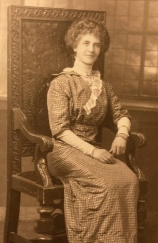 Victorianwoman sat in a large wooden chair, wearing a dress with frills. The image is in black and white.