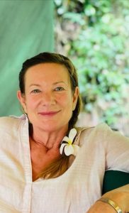A portrait photograph of Harriet Forde, with her plaited and a flower at the end, wearing a white shirt, with greenery in the background.