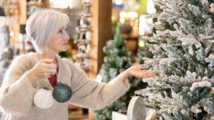 An older woman hanging up a bauble on a Christmas tree.