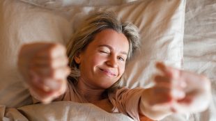 Woman lying in bed stretching in the morning. How to get to sleep and which hacks to avoid.