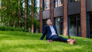 A mature businessman resting and sitting barefoot in park, feeling free, escaping from work, work life balance concept.