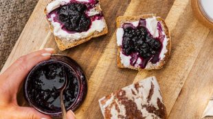 A jar of jam beside three slices of bread, currently being spread with the jam