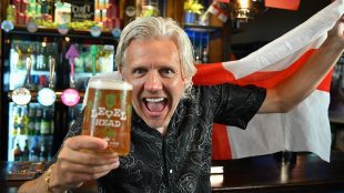 Image shows football figure Jimmy Bullivant in a pub with a cold pint of beer, waving an England flag