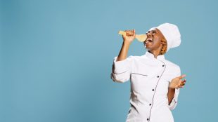 A woman singing into a wooden spoon on a blue background