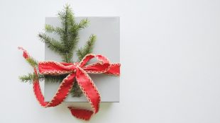 A box sits on a white table with a red ribbon around it and green folliage tucked into the ribbon. Last Christmas posting dates UK