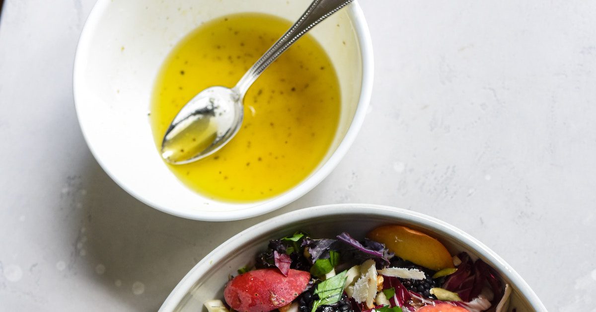 White bowl with salad dressing in and a silver spoon.