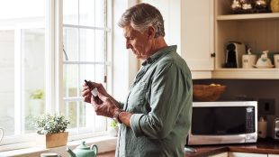 CBD/THC oil, tea and a senior man in the kitchen for his morning medication routine. Thinking, medical cannabis and dose with a mature man holding a medicine bottle in his house. Medical cannabis helpfing older people in UK - article Silver Magazine www.silvermagazine.co.uk