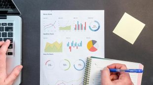 A sheet of charts between a laptop and a notebook where someone writes. Planning retirement finances
