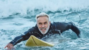 Surf, sea and sports with a mature man surfer in the water for sport, fitness and surfing during summer. Fitness and exercise with a male athlete on his surfboard in the ocean alone. New supplement for joint pain - sponsored article Silver Magazine www.silvermagazine.co.uk