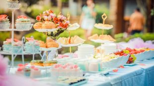 Well decorated cakes displayed on a long table in a back garden. Best garden party tips Silver - www.silvermagazine.co.uk