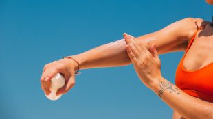 Outstretched arm against a blue sky as the person applies lotion to their arm. Silver's summer beauty edit