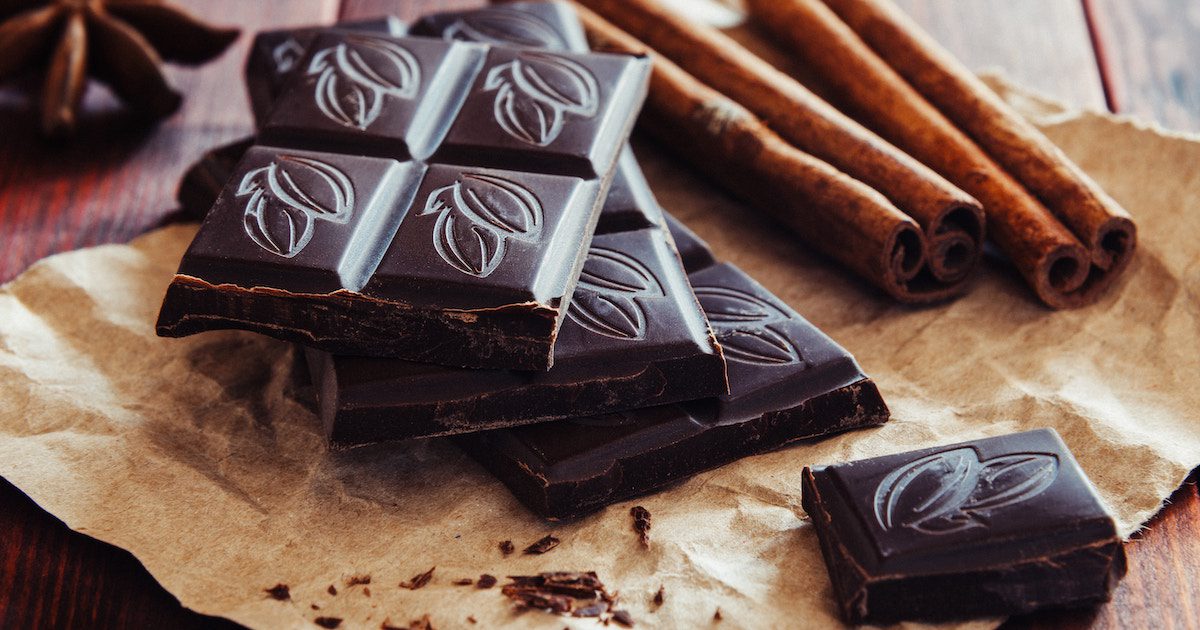 A stack of dark chocolate on brown paper, which two sticks of cinnamon behind. Benefits of dark chocolate on Silver Magazine.