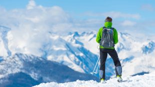 Person standing on top of a snowy mountain looking out across the peaks. Reasons to start skiing article on Silver Magazine www.silvermagazine.co.uk