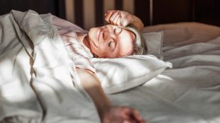 Happy fresh mature middle aged woman stretching in bed waking up alone happy concept, smiling lady awake after healthy sleep sitting in cozy comfortable bedroom interior enjoy good morning. Remedies for insomnia perimenopause - article Silver Magazine www.silvermagazine.co.uk