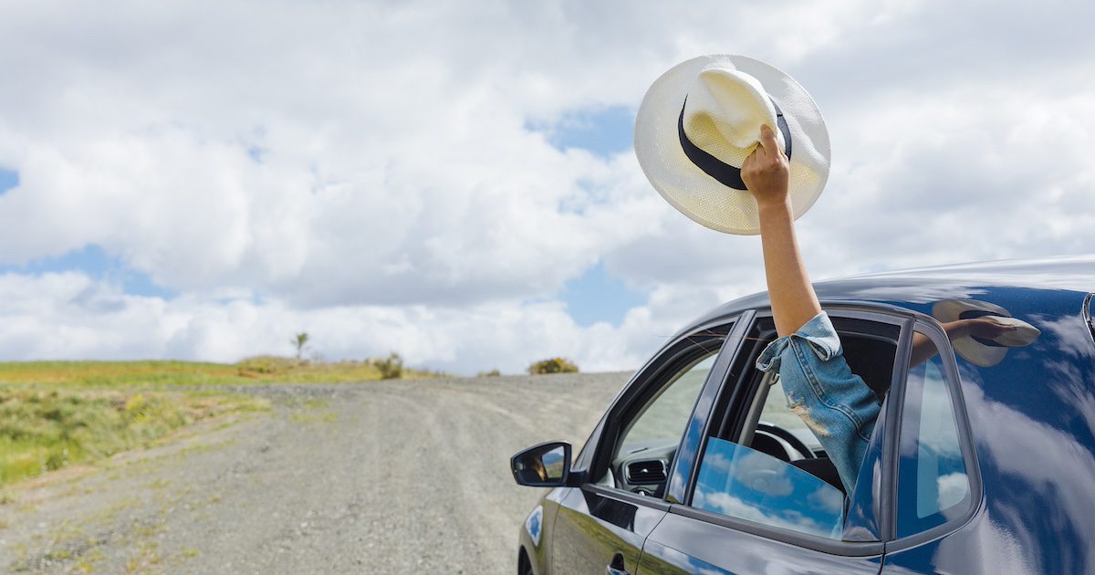 Car driving along with someones arm coming out holding a hat