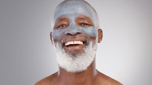 Skincare, clay mask and portrait of black man with smile, happiness and anti ageing treatment on studio background. Dermatology, cosmetic grooming and happy, mature model in charcoal skin care facial. Self care for confidence article Silver Magazine www.silvermagazine.co.uk