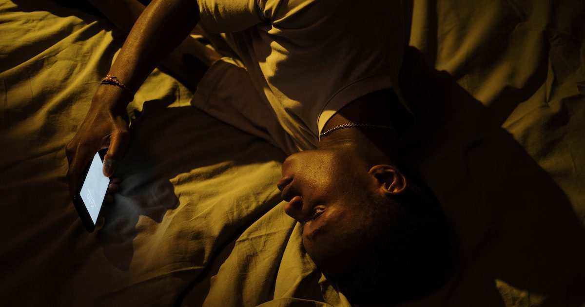 Person lying in bed in the dark looking at their lit up phone