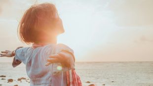 Woman happy and carefree on a beach, sunlight etc. Stop negative thoughts article Silver Magazine www.silvermagazine.co.uk