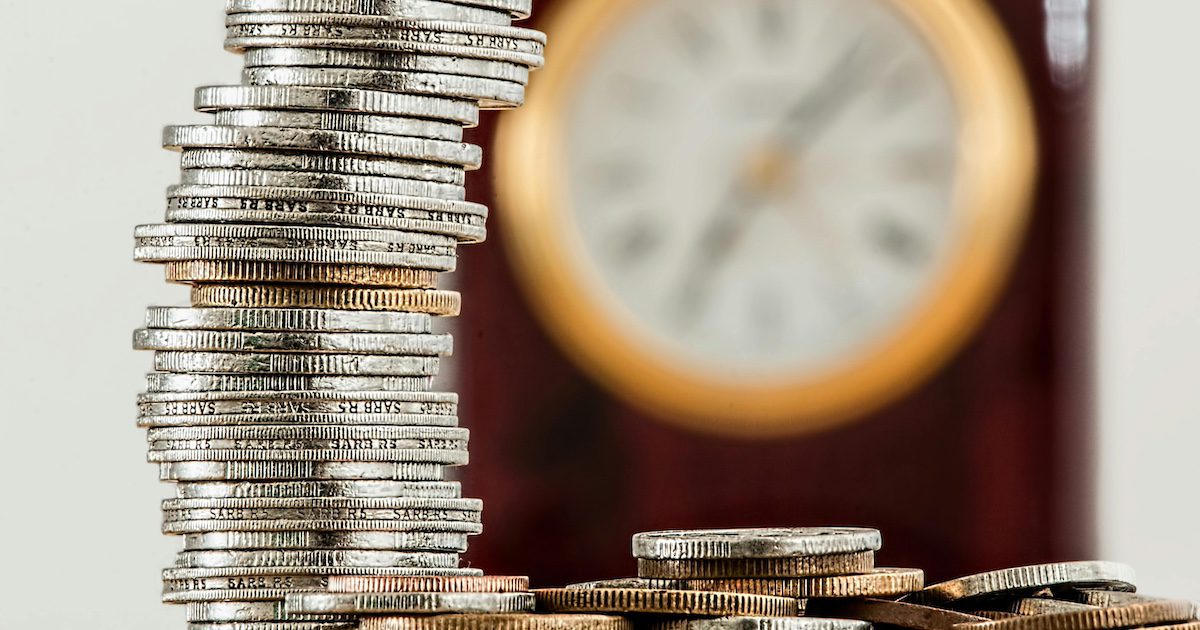 Stack of coins on table in front of a clock