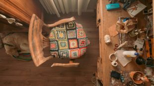 room with a chair featuring a hand-sewed seat cover in the centre of a frame with a golden labrador sat just behind it on a wooden floor. it is a top down shot. in front of the table is a desk with assorted craft supplies on it. TM1566-SIL-Header-Image-Why-building-a-hobby-room-will-spark-joy-silvermagazine-silvermagazine.co_.uk_.jpg