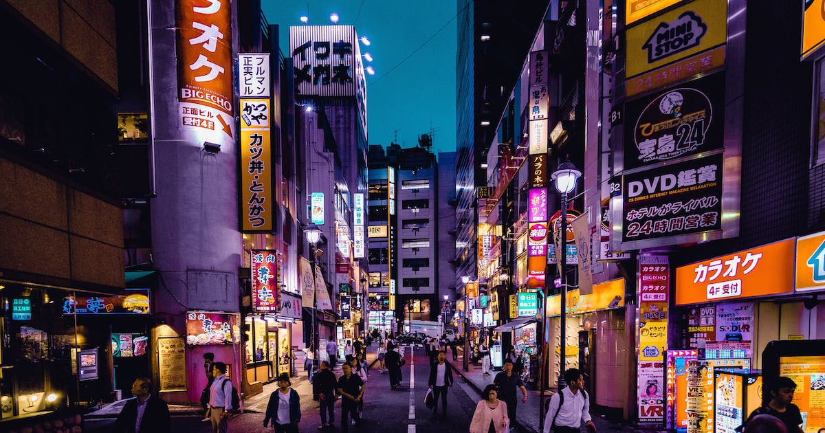 Busy Tokyo street in late evening light, with lit up shop signs.
