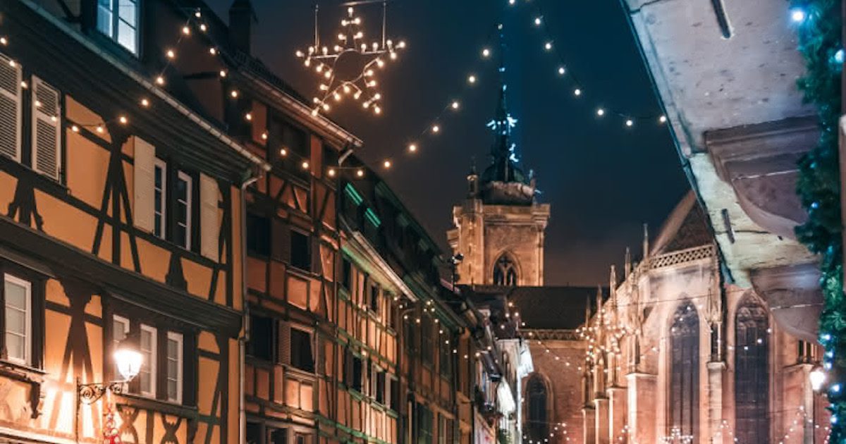 Christmas lights against a dark night sky and traditional buildings of Colmas, France. Ultimate Christmas market guide on Silver