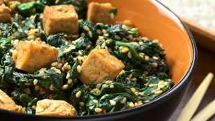 Image shows bowl of asian inspired tofu with spinach and sesame seeds sprinkled on top, with chopsticks resting at the side