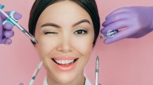 Portrait of a beautiful winking woman and many syringes with beauty injections around her face. WHy should dentists and nurses do a botox course - Silver Magazine www.silvermagazine.co.uk