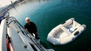 Mature gentleman pouts at the camera whilst standing on the side of a boat suspended above aquamarina waters. You're never too old
