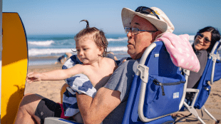 Two grandparents sitting on the beach with their grandchild.
